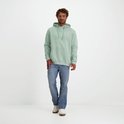 Staande man in mintgroene hoodie met logo en jeans op een witte achtergrond.