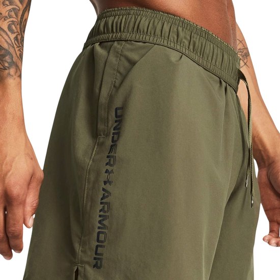 Legergroene shorts met verticale zwarte Under Armour-letters op de linkerpijp