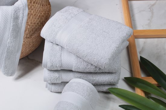 Stapel lichtgrijze handdoeken, de bovenste is gevouwen. De textuur is zacht en de randen hebben een decoratief patroon.