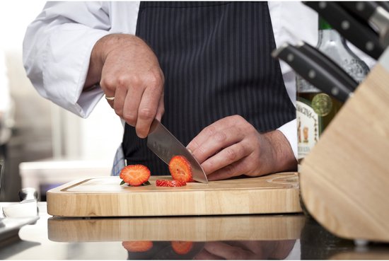 Chef snijdt aardbeien op een houten snijplank.