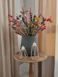 Twee gouden geometrische kandelaars met LED waxinelichtjes op een houten tafeltje, voor een vaas met droogbloemen.