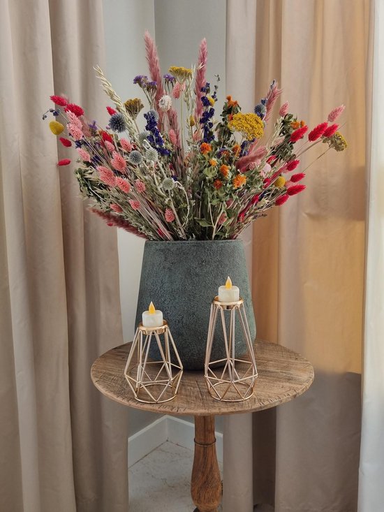Twee gouden geometrische kandelaars met LED waxinelichtjes op een houten tafeltje, voor een vaas met droogbloemen.
