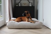Bruine boxer die ontspannen ligt op een rond, lichtbeige hondenkussen met wafelpatroon.