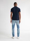 Man, van achteren gezien, draagt een marineblauwe polo en een lichtblauwe slim fit jeans met lichte wassing.