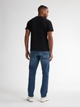 Man met de rug naar de kijker, draagt een zwarte t-shirt en een blauwe jeans. Witte sneakers.