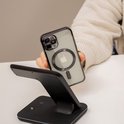Hand toont transparant telefoonhoesje met MagSafe-ring op een zwarte draadloze oplader.
