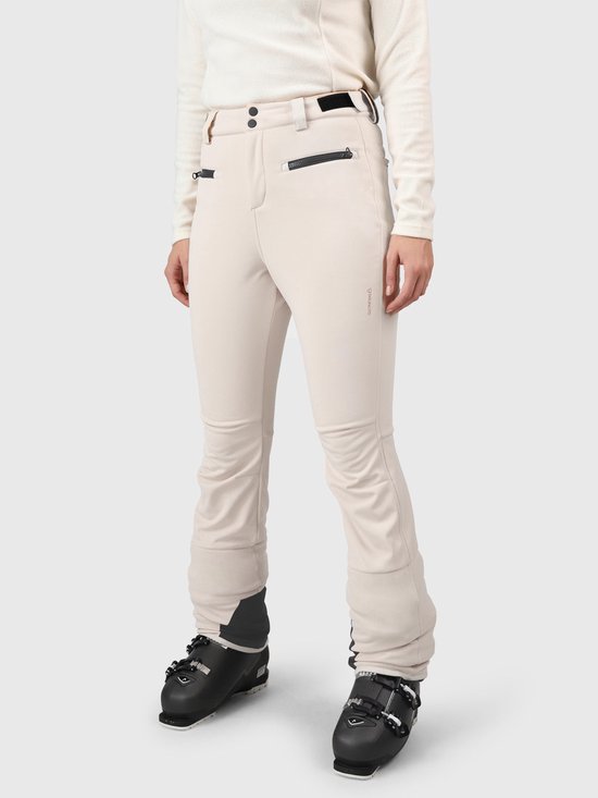 Model van voren in een beige skibroek met zwarte accenten en ski-uitrusting.