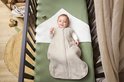 Baby ligt in een wieg in een beige slaapzak, glimlacht naar de camera.