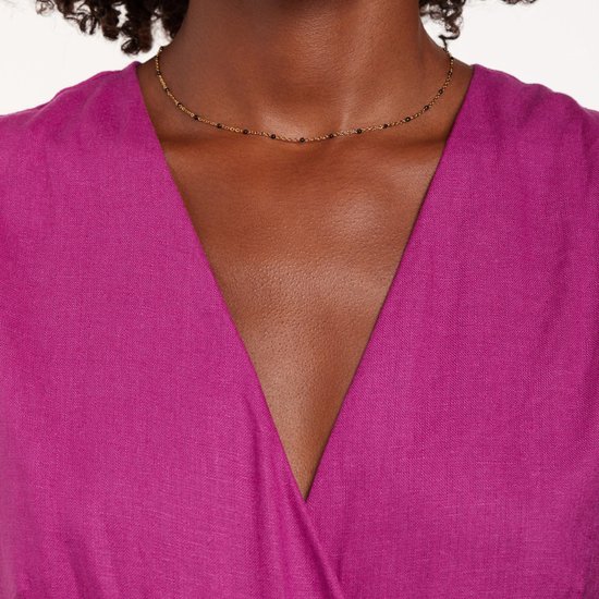 Hals van model met gouden ketting met zwarte kraaltjes.