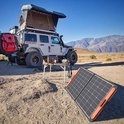 Off-road voertuig met daktent, Jackery Explorer 1500 krachtcentrale en opvouwbaar zonnepaneel op rotsachtig terrein met bergen op achtergrond.