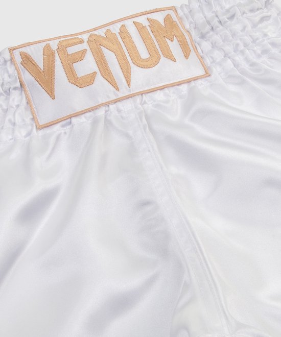 Witte Muay Thai broek van satijn met gouden VENUM logo op een patch bij de tailleband.