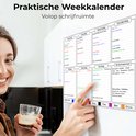 Een vrouw met een drankje lacht terwijl ze naar de magnetische weekplanner op de koelkast kijkt. Planbord met secties voor dagen, boodschappenlijst en notities.
