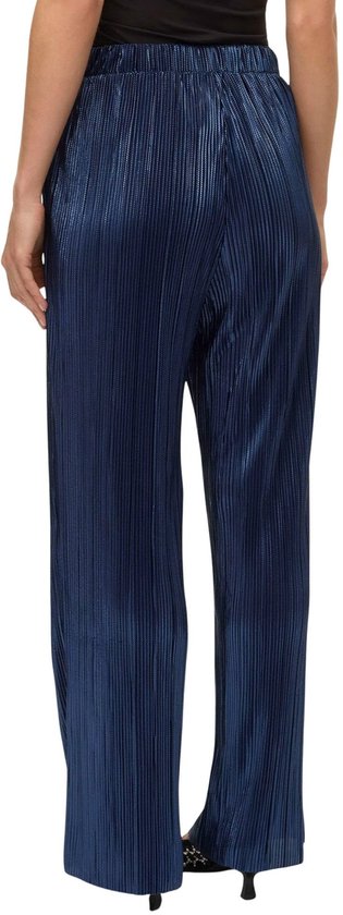 Model draagt een donkerblauwe, glanzende, geplooide broek met wijde pijpen.