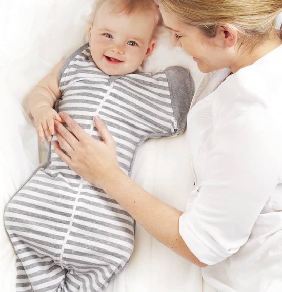 Baby in grijs gestreepte Swaddle Up met armen omhoog, met een hand op zijn borst.