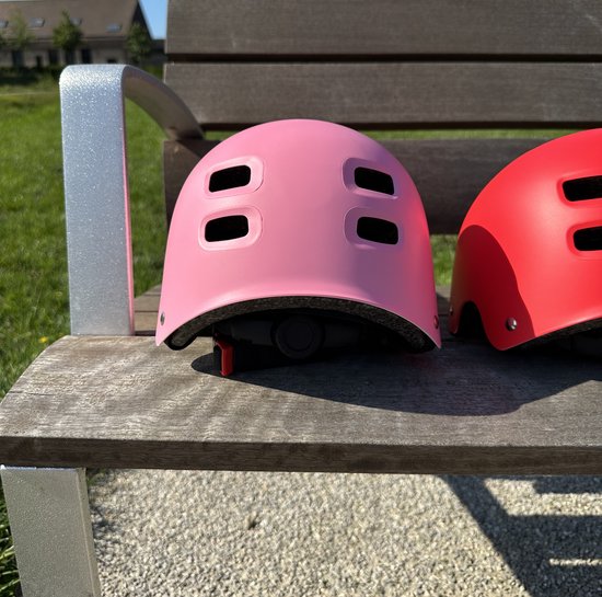 Casque rose avec aérations, sur un banc en bois.