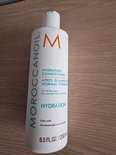 Witte Moroccanoil Hydrating Conditioner fles met oranje M-logo op een houten ondergrond.