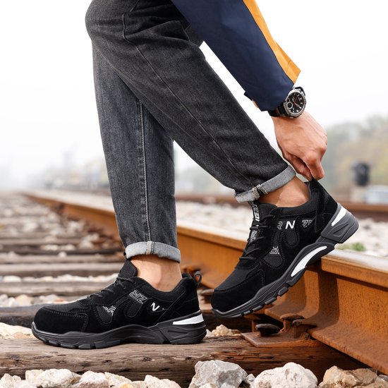 Man draagt zwarte NezR werksneakers met witte accenten op een spoorlijn.