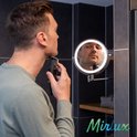 Man scheert zijn baard met elektrisch scheerapparaat voor een badkamerspiegel met LED verlichting.