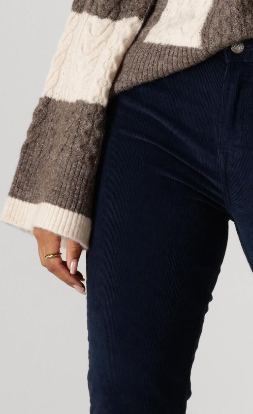 Model draagt een donkerblauwe corduroy broek en een gebreide trui met strepen.