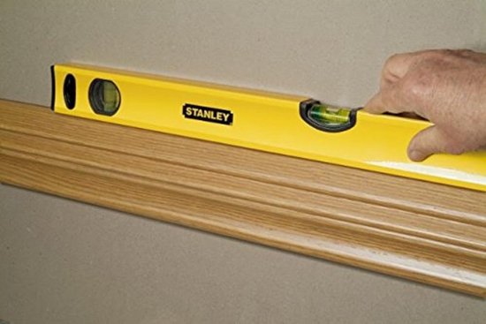 Gele Stanley waterpas met bubbelnivelleerder op een houten lijst.