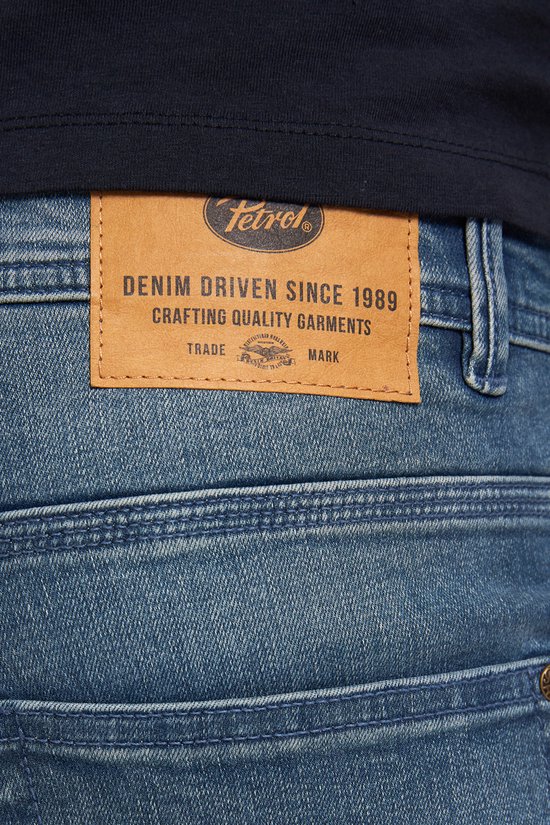 Leren label op de achterkant van een spijkerbroek met de tekst 'Petrol Industries' en 'Denim Driven Since 1989'.