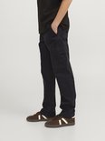 Zij-aanzicht van een jongen in zwarte cargo broek en bruine sneakers. Hand in broekzak.
