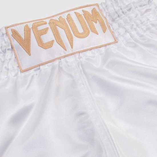 Witte Muay Thai broek van satijn met gouden VENUM logo op een patch bij de tailleband.