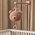 Lichtbruine teddybeer-muziekhanger hangend boven een kinderbedje.