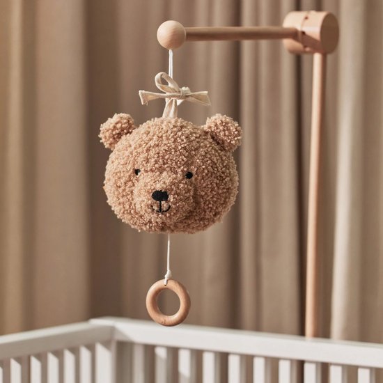 Lichtbruine teddybeer-muziekhanger hangend boven een kinderbedje.