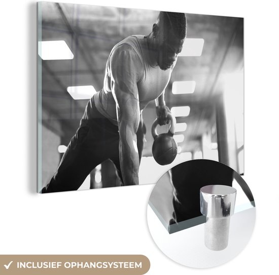 MuchoWow® Glasschilderij 60x40 cm - Schilderij acrylglas - Een sterke man tilt tijdens fitness kettlebells omhoog - zwart wit - Foto op glas - Schilderijen