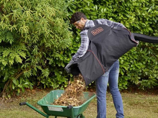 Man met rugzak-opvangzak leegt bladeren in een groen-grijze kruiwagen.
