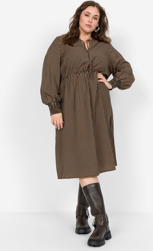 Model draagt een bruine jurk met zwarte strepen, pofmouwen, smockdetails bij de polsen en donkerbruine laarzen.