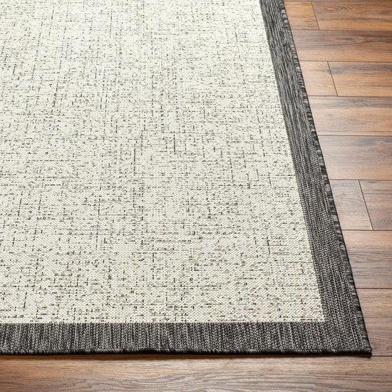 Tapis couleur crème avec des lignes géométriques gris-noir et une bordure gris foncé, sur un plancher en bois.