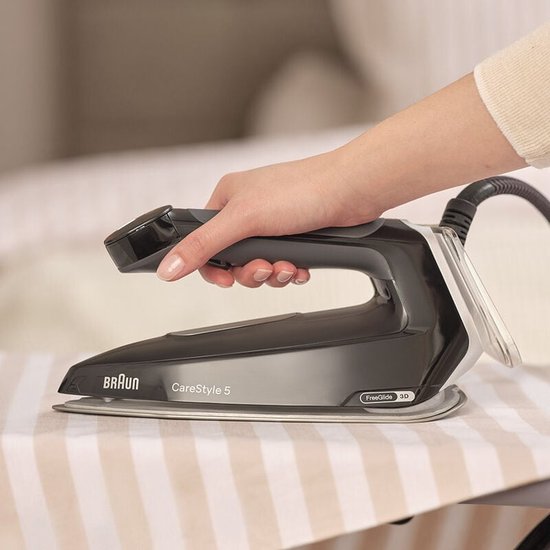 Hand strijkt met zwart Braun CareStyle 5 strijkijzer op een gestreept strijkplankovertrek.