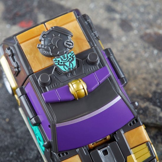 Close-up van een speelgoedauto in voertuigmodus. Zwart met gouden en paarse details, met een Decepticon-logo.