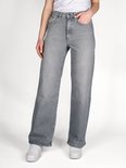 Model in een grijze jeans met wijde pijpen, hoge taille en witte sneakers.