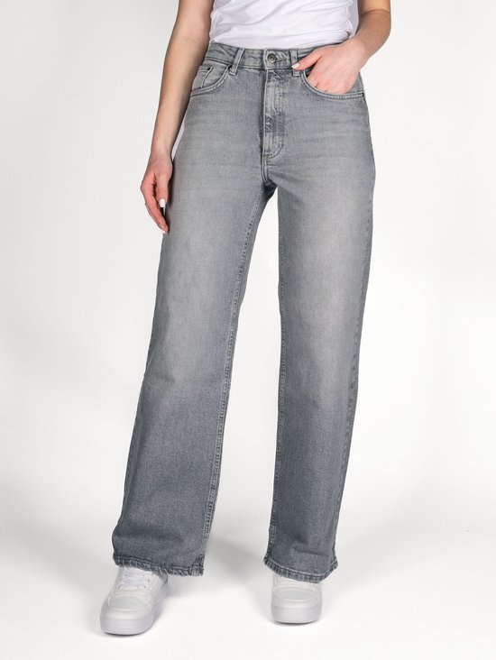 Model in een grijze jeans met wijde pijpen, hoge taille en witte sneakers.