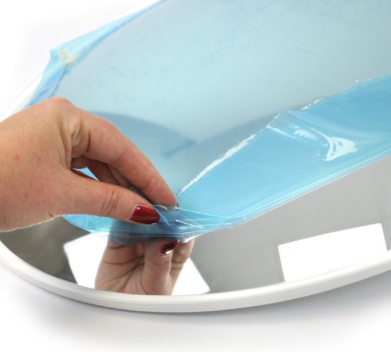 Hand trekt blauwe beschermfolie van spiegel met witte rand.