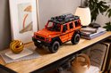 Oranje LEGO Technic Mercedes-Benz G 500 model op een houten tafel naast een lamp en abstracte decoratie.