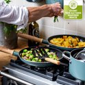 Frituren van groenten in een koekenpan met houten handgreep op een gasfornuis. Een groene sticker toont een kookplaat met 'Geschikt voor alle vuren waaronder inductie'.