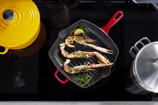 Gegrilde langoustines met citroen en kruiden in een rode gietijzeren grillpan op een kookplaat.