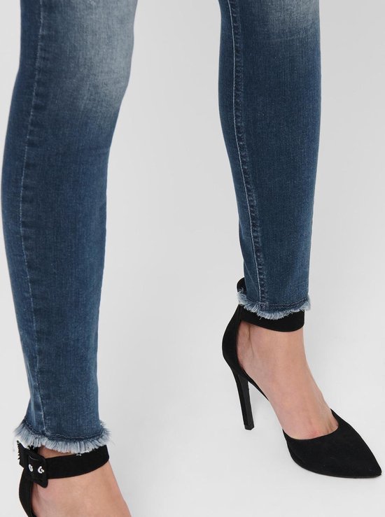 Close-up van de enkel van een vrouw in een spijkerbroek met rafelige zoom, met zwarte pumps met enkelbandje.