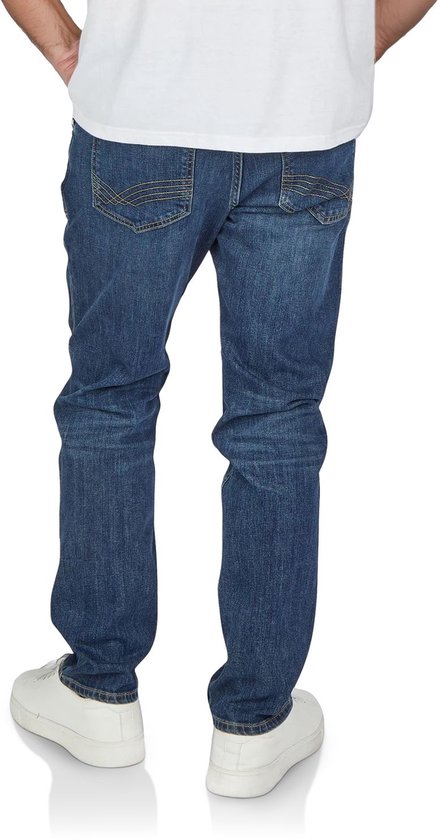 Een man in een blauwe regular fit jeans, staand, van achteren gezien, met witte sneakers.