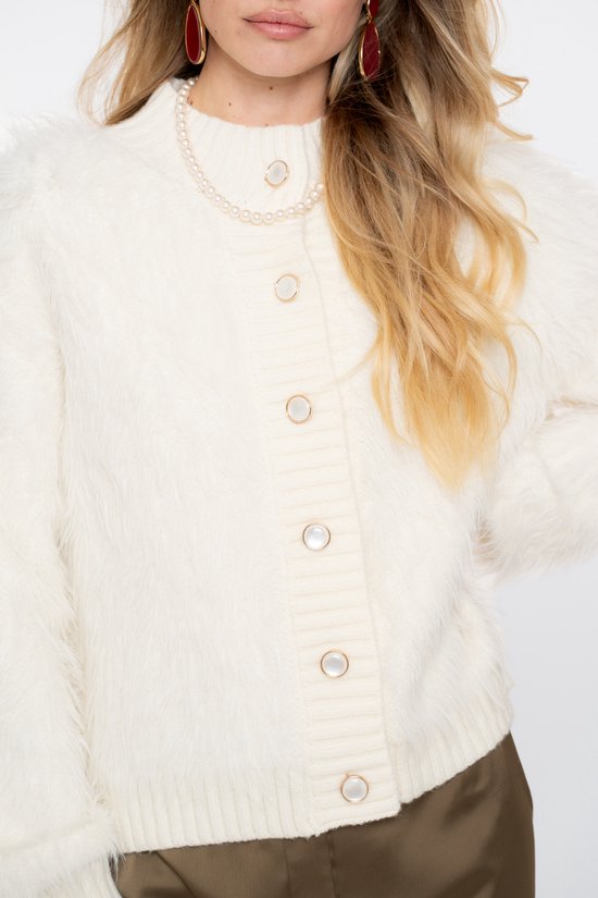 Close-up van een off-white, harig vest met knoopsluiting en parelketting op een model.