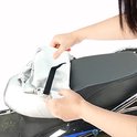 Handen bevestigen een zilverkleurige zadelhoes aan een zwart scooterzadel.