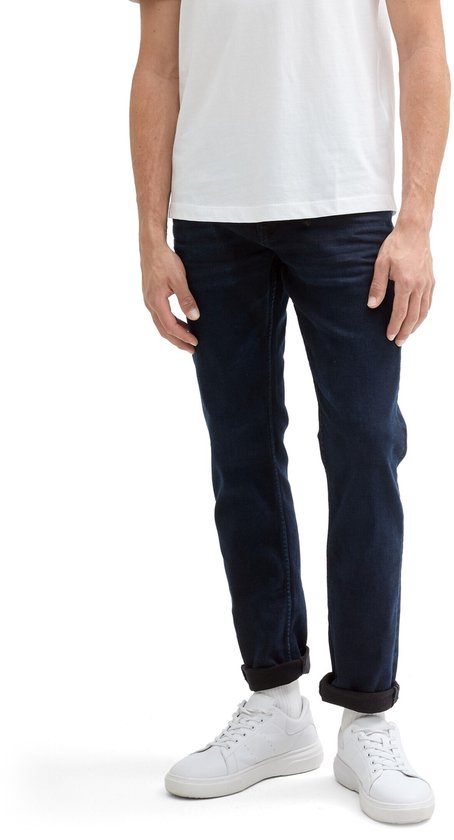 Man in een donkerblauwe slim fit jeans, witte sokken en witte sneakers.