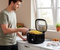 Man met groene trui gebruikt zwarte Tomado friteuse met mand vol goudgele frietjes.