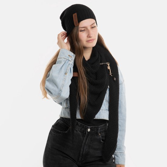 Vrouw in denim jas, zwart shirt, zwarte jeans en zwarte gebreide sjaal en muts, witte achtergrond.