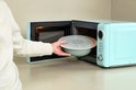 Hand plaatst een lichtgroene Mepal ronde kom met transparant deksel in een mintgroene magnetron.