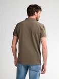 Rugzijde van een man in een olijfgroen poloshirt en blauwe jeans, gezien vanaf de achterkant.